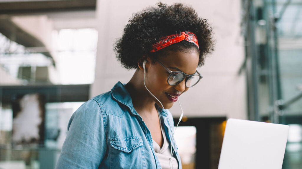 Smiling young African female university student sitting on a campus bench working on a laptop while preparing for an exam