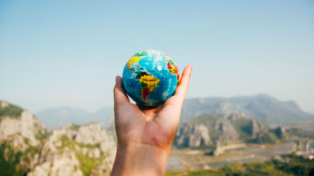 Hand holding a small globe with mountain scenery behind