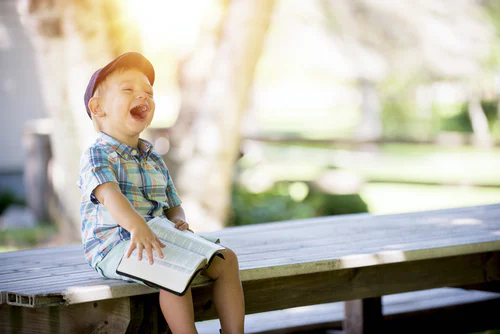young boy reading on a picnic table, laughing