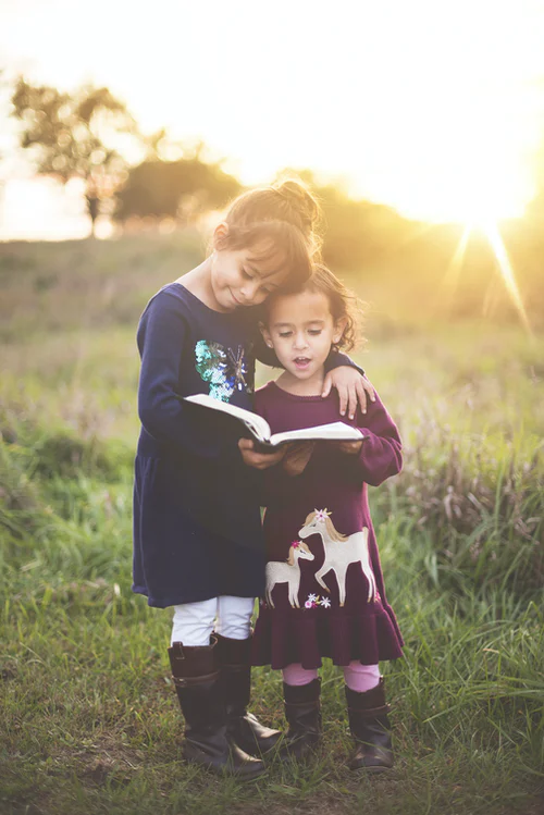 two young girls reading a book in a field