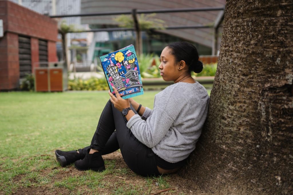 girl reading book against a tree