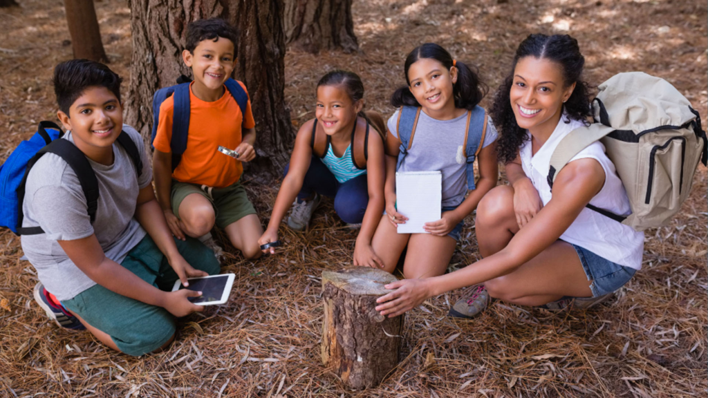 Students and teacher crouching under a tree.