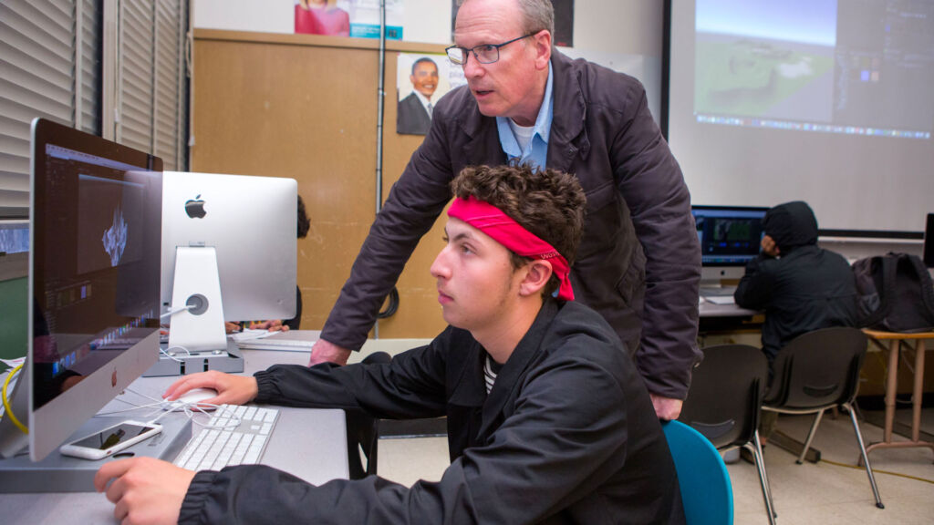 Teacher helps a student at the computer.