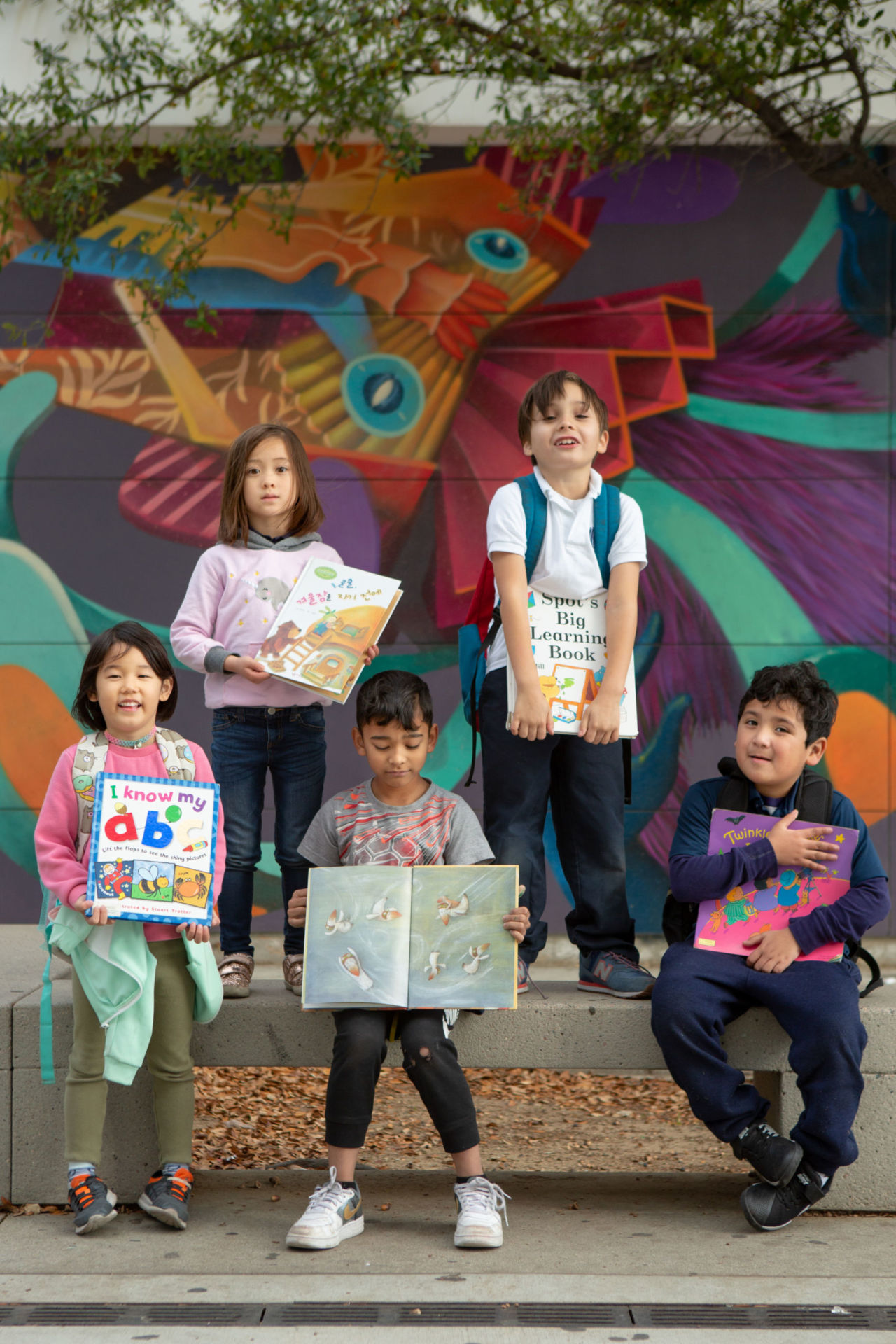 Elementary students with books and school mural