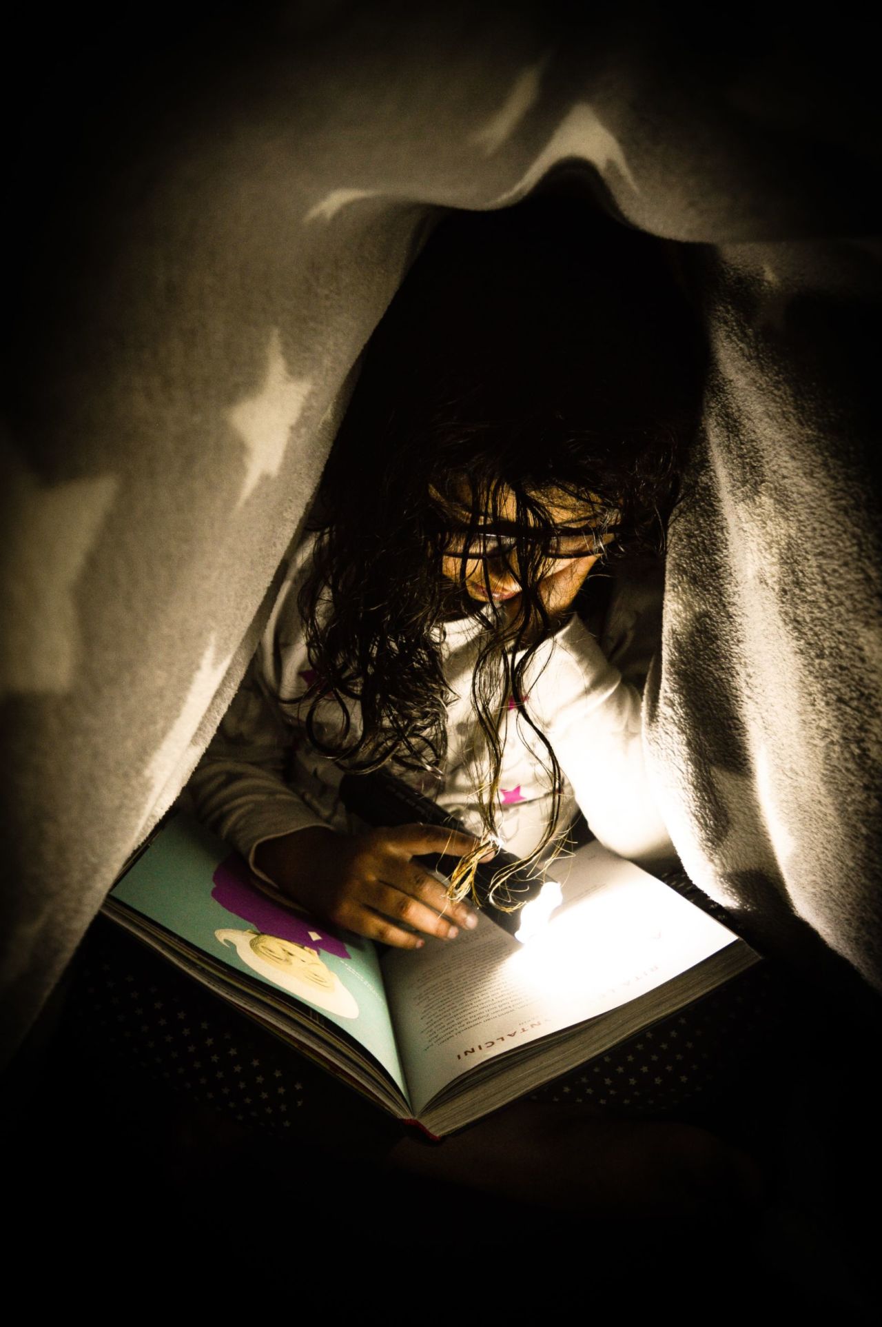Student reading under a blanket.