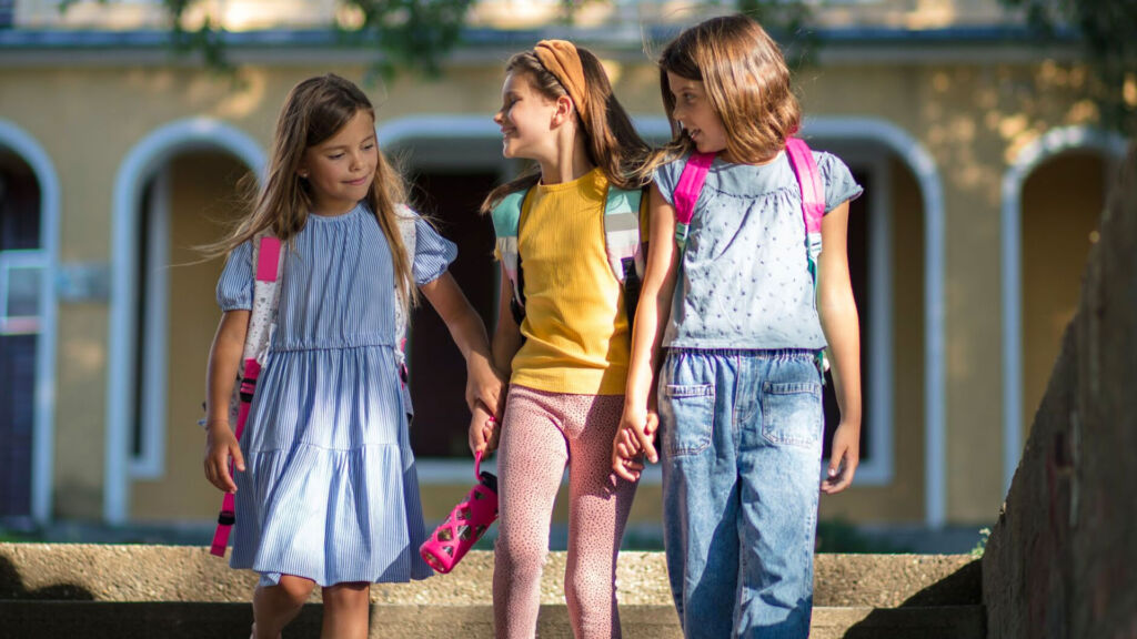 Three students holding hands outside.