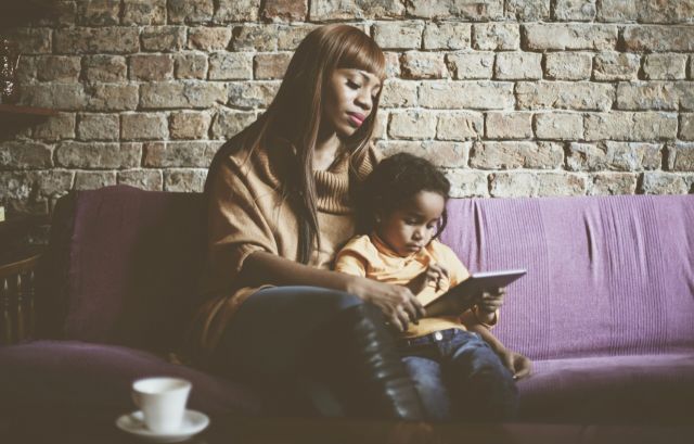 Mother and child reading a book, sitting on a couch.