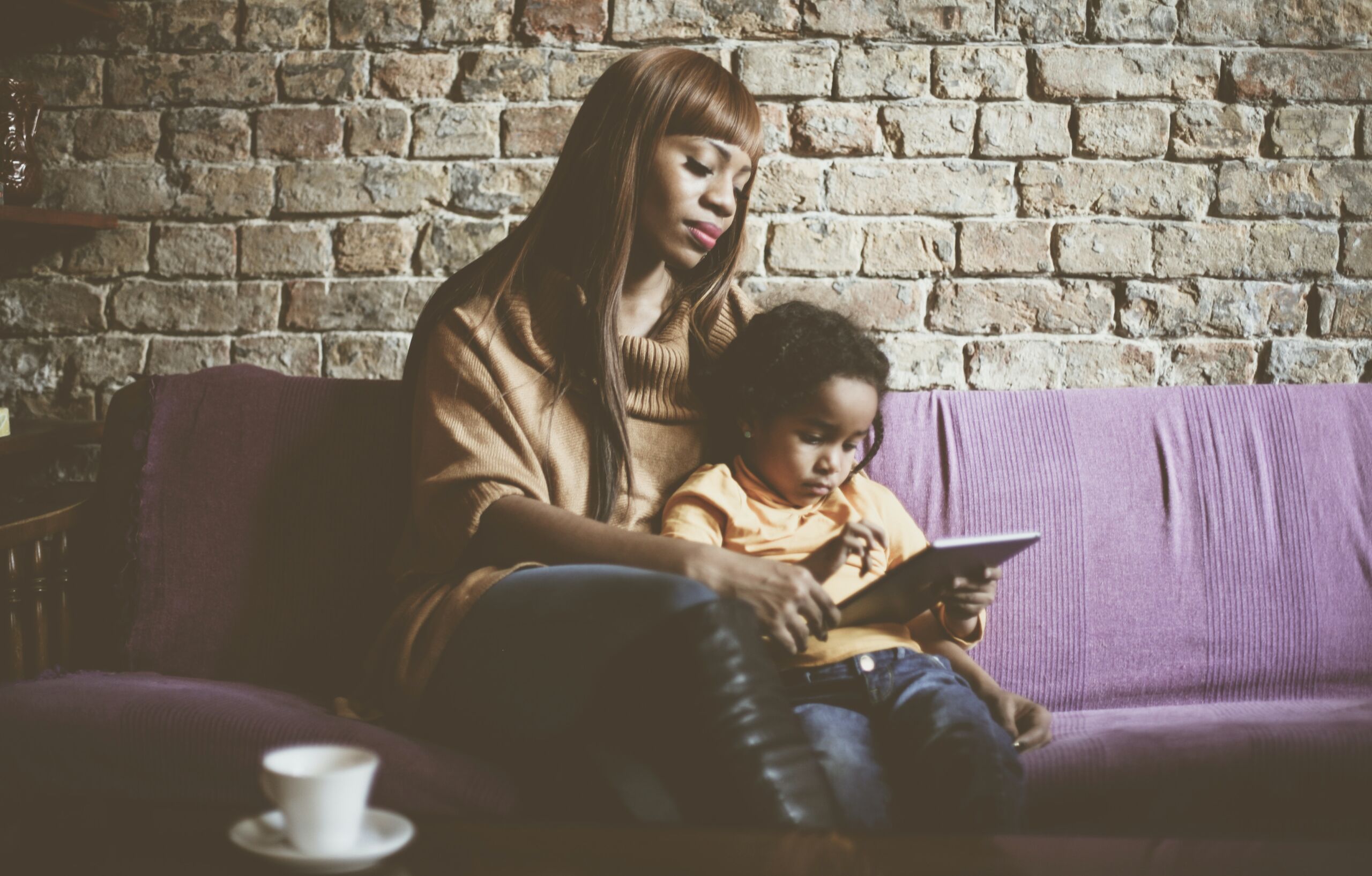 Mother and child reading a book, sitting on a couch.
