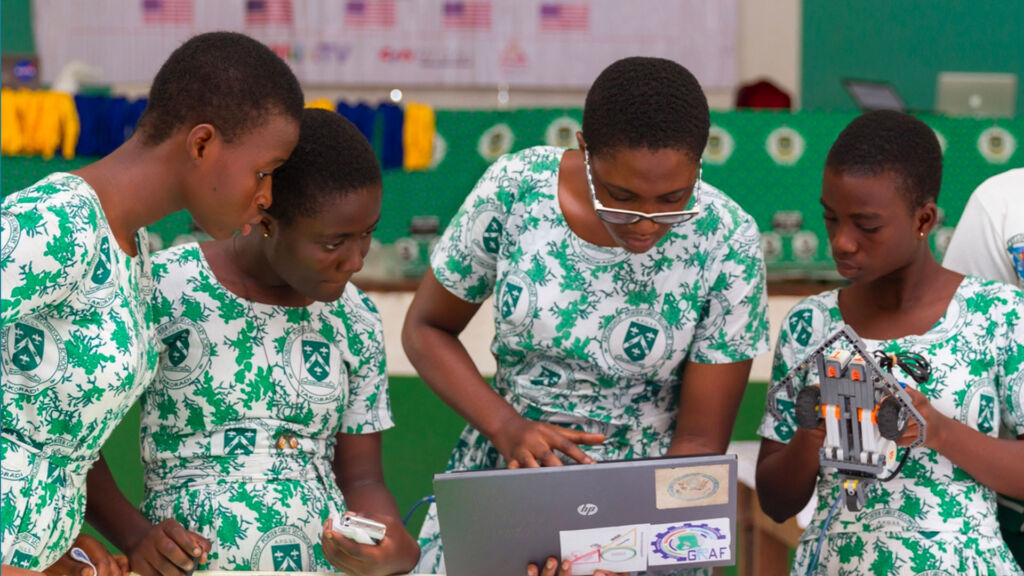 A teacher and students working together on a laptop.