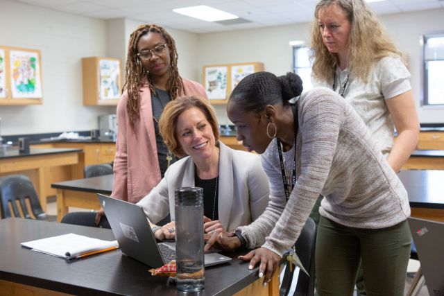 Teachers and students looking at a laptop in a classroom.