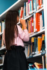 Student looking at books on a library shelf.