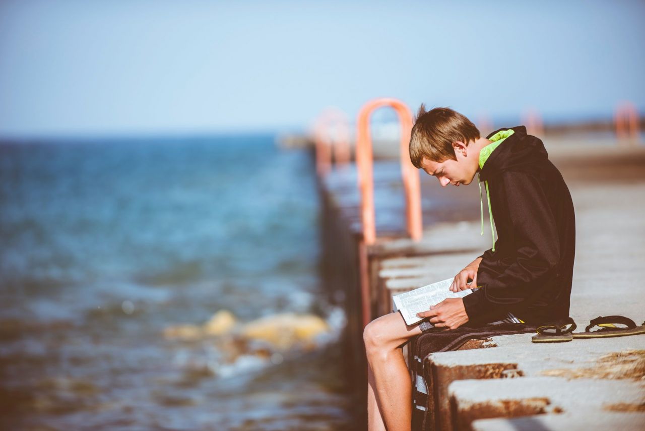 Boy sitting on a dock with a book.