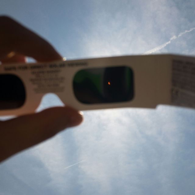Person holding eclipse glasses in the air.