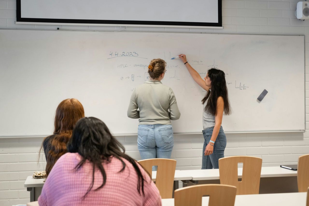 Teachers writing on the whiteboard, while students look on.