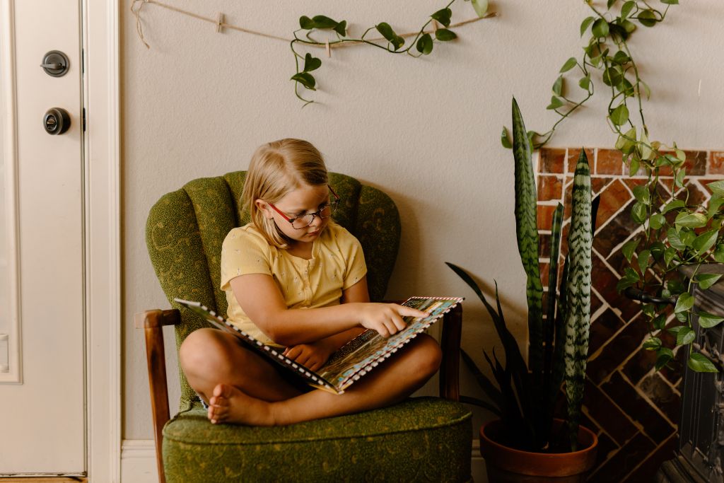 Girl sitting in a chair, reading a book.