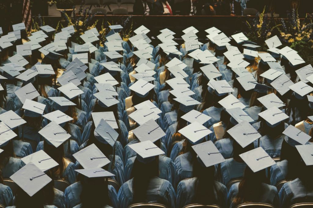 People in graduation outfits, sitting down and waiting.