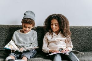 Two children sitting on a couch and reading.