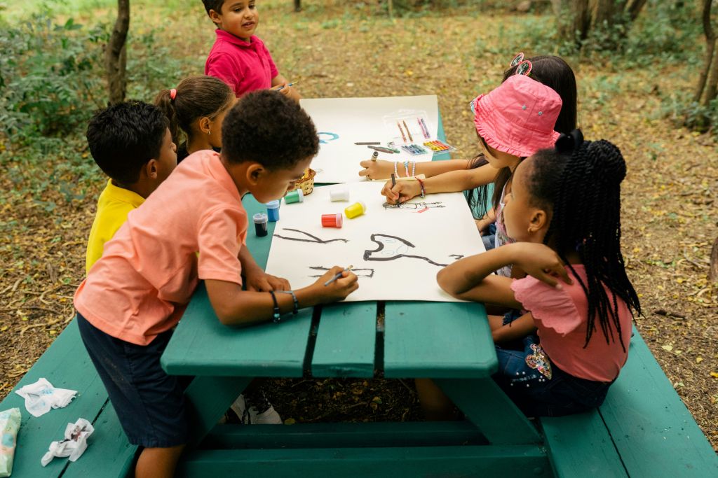 Children sitting together, working on artwork, and a picnic table.