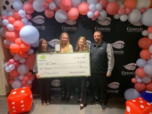 Four people holding a large check under a balloon arch.