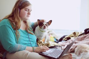 Student using a laptop with a dog standing nearby.