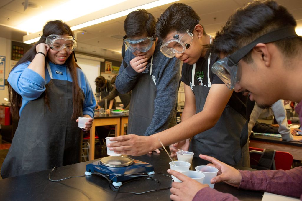 Three high school boys and one high school girl work together on an experiment in AP chemistry class.