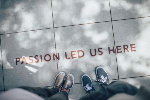 Two people standing on gray tile paving with the words, "Passion led us here."