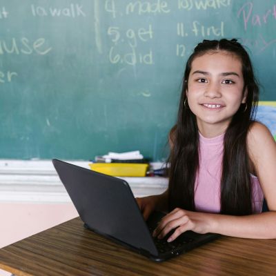 Female student sitting with her laptop, at a desk, in the classroom.