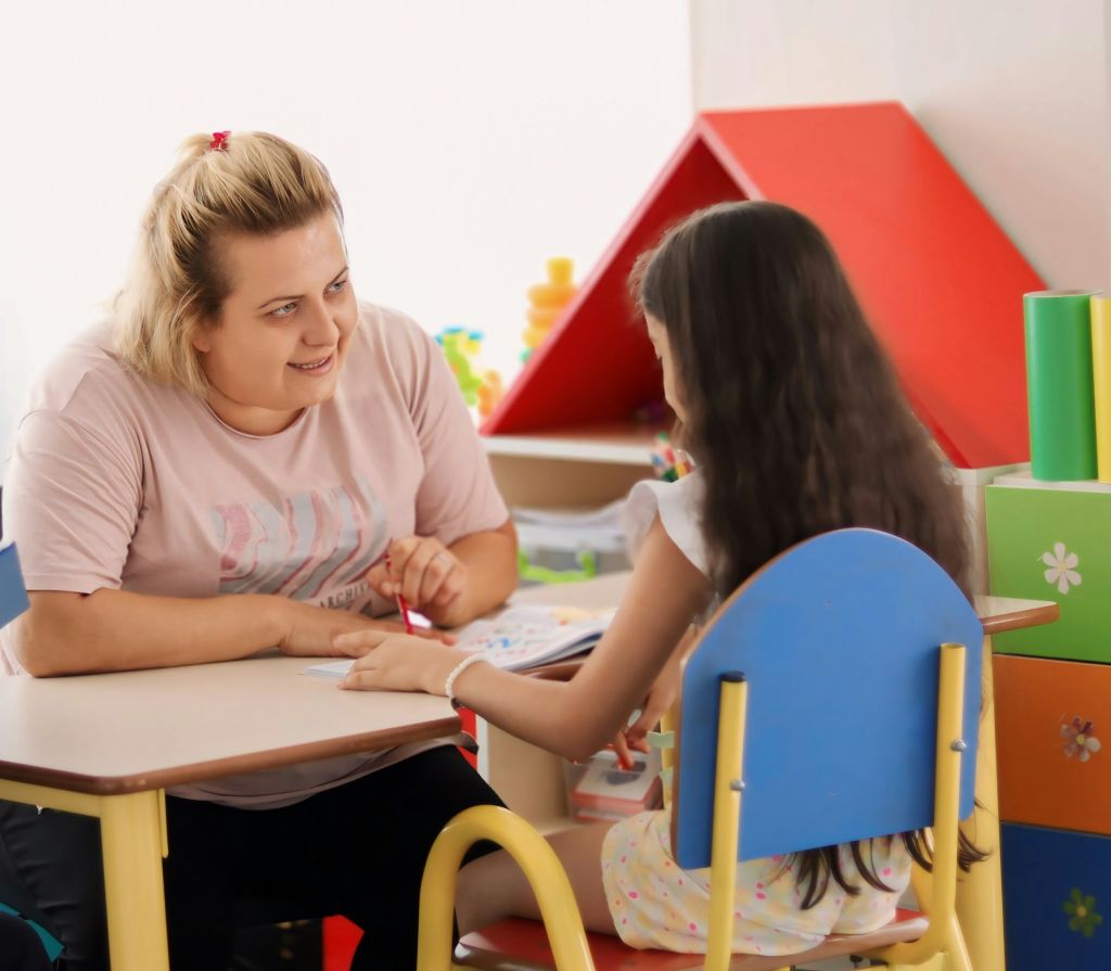 Smiling adult talking to a student while sitting together at a table