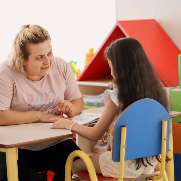 Smiling adult talking to a student while sitting together at a table