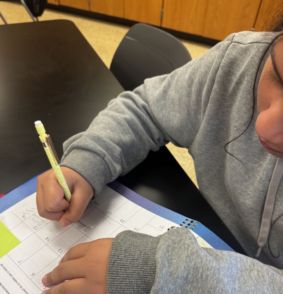 student writing on paper while seated at desk