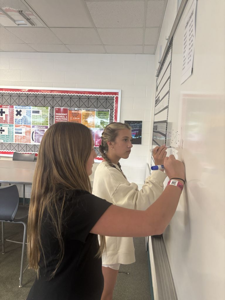 2 middle school girls working at a white board