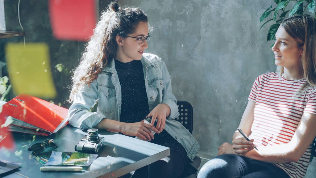 Two women sitting near a chalkboard talking