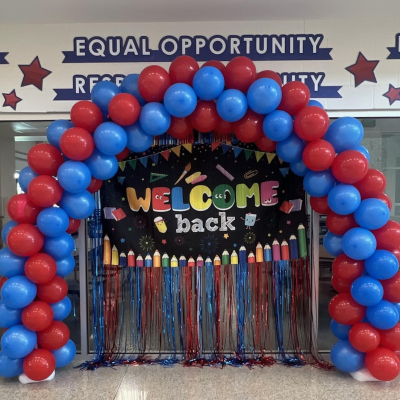 A red & blue balloon over a "Welcome Back" sign